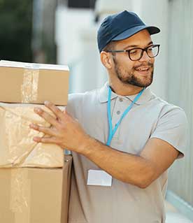 A delivery driver in a cap and lanyard carrying stacked cardboard boxes