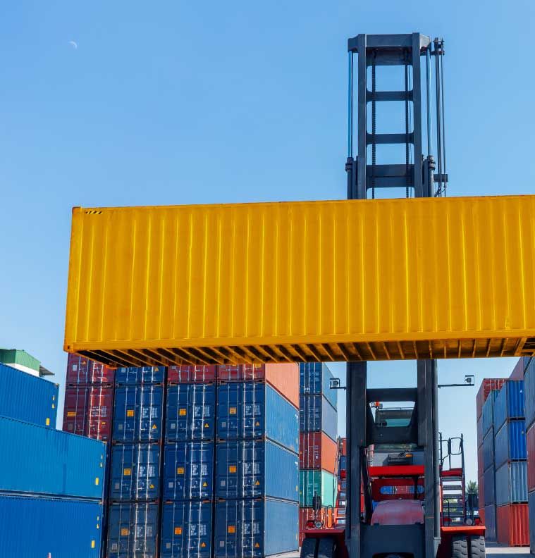 A reach stacker lifting a yellow shipping container above a stacked container yard