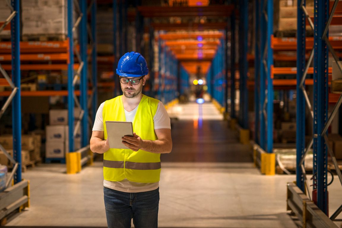 A worker walking through a large storage warehouse using a tablet